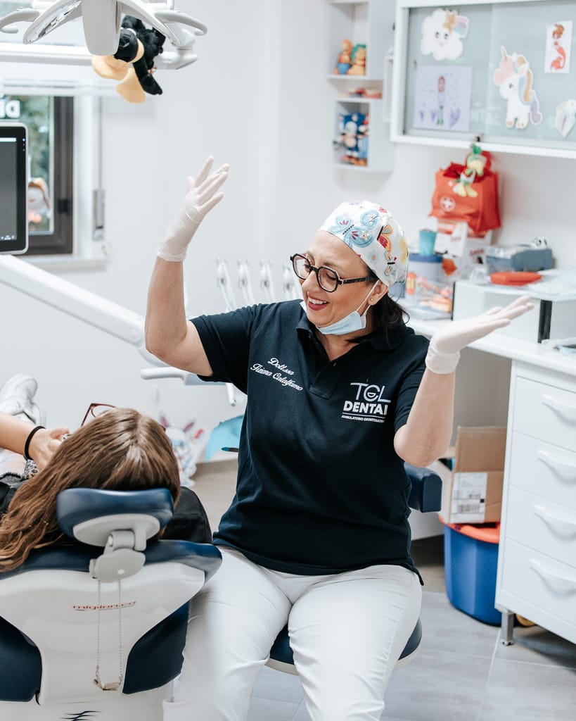 La Dott.ssa Tiziana Catalfamo alza le braccia e ride accanto a una bambina seduta sulla poltrona, nella sala di TCL Dental a Barcellona Pozzo di Gotto