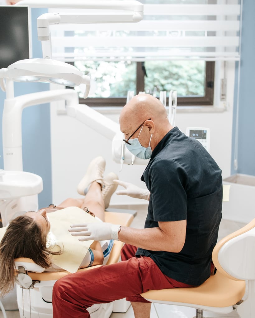 Il Dott. Ignazio D'Anna seduto accanto al riunito con una paziente adulta distesa, nella sala luminosa di TCL Dental