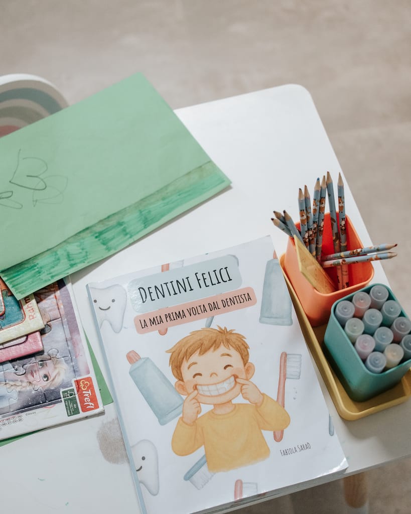 Il libro illustrato "Dentini Felici", sulla prima volta dal dentista, sul tavolo accanto a un portapenne con matite colorate