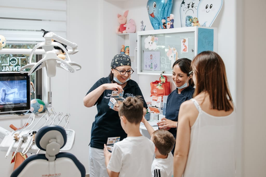 La Dott.ssa Tiziana Catalfamo consegna un regalo a due bambini accompagnati dalla mamma, nella sala di TCL Dental