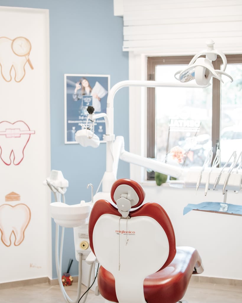 Riunito con poltrona rossa e parete azzurra decorata con illustrazioni di denti, sala di TCL Dental