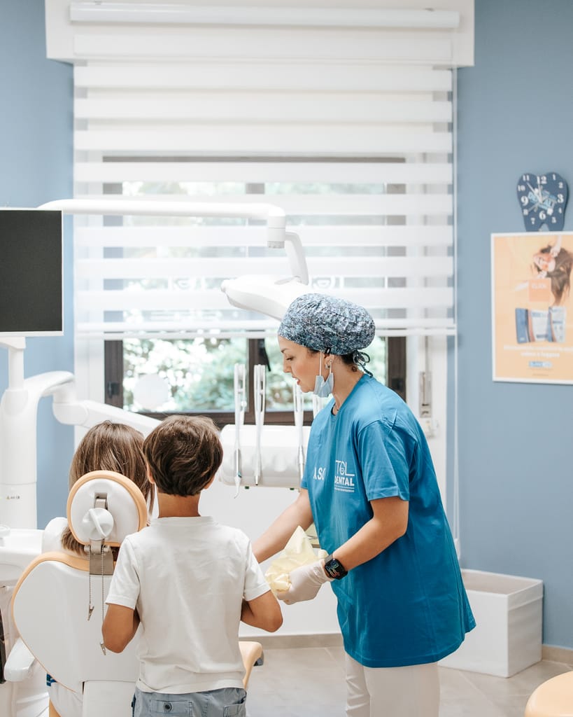 Sala di TCL Dental con pareti azzurre e grande finestra, un'assistente accompagna due bambini verso il riunito