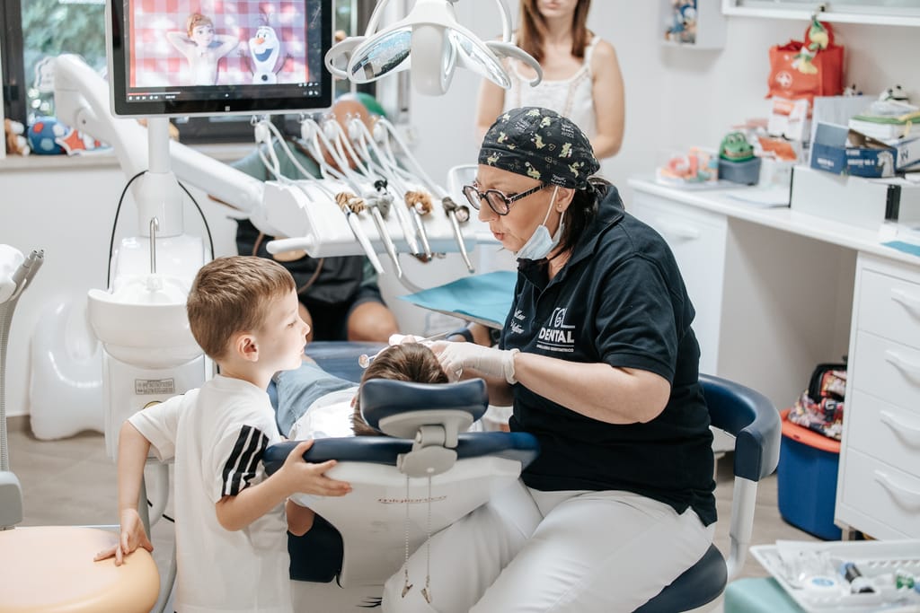 Un bambino in piedi guarda la sorella seduta sul riunito mentre la Dott.ssa Tiziana Catalfamo la visita, TCL Dental